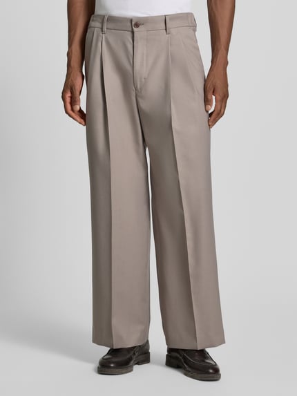 Männermodel trägt Wide Fit Hose mit Bügelfalten von Drykorn aus Baumwoll-Mix mit Stretch-Anteil in Beige, Nahaufnahme Vorderansicht.