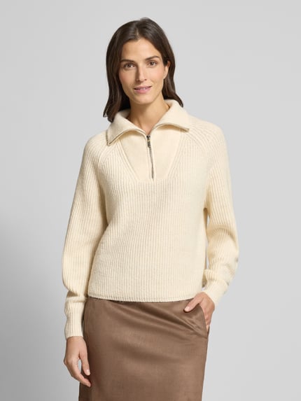 Modelka kobieca nosi Regular Fit Pullover mit Woll-Alpaka-Anteil Modell 'Poy' od OPUS w kremowym kolorze o fakturze dzianiny, z trojerem, widok na górną część ciała z przodu. Pulower wykonany z mieszanki materiałów z dodatkiem wełny i alpaki, długość tyłu 57 cm, długość rękawa 79 cm, fason regular.