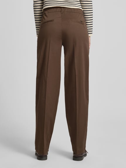 Frauenmodel trägt Chino mit Bügelfalten von Brax aus Baumwoll-Mix mit Lyocell-Anteil, regular Fit, braun, Ziertaschen, Ganzkörperansicht Rückansicht.