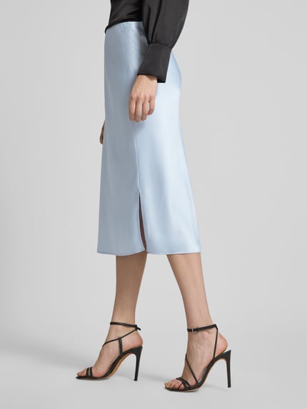 Kobiece modelka nosi spódnica midi z satyny z bocznymi rozcięciami Midirock aus Satin mit Seitenschlitzen von Calvin Klein Womenswear, prosty krój, elastyczny pas, szerokość w rozmiarze S 41 cm, całkowita długość w rozmiarze S 76 cm, jasnoniebieska, satynowa powierzchnia, całkowity widok z boku