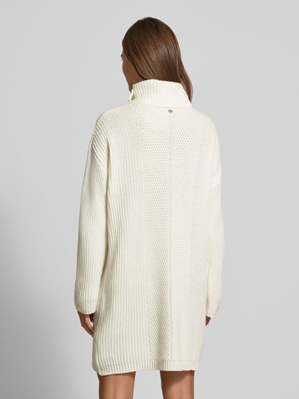 Frauenmodel trägt Strickkleid mit Rollkragen von Liu Jo White in Creme, Material-Mix mit Woll-Anteil, gerader Schnitt, Minikleid, Rückenlänge 88 cm, Brustweite 52 cm, Ärmellänge 54 cm, grobe Textur, Knopfdetails, Ganzkörperansicht Rückansicht.