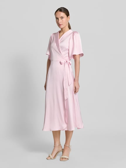 Modelka kobieca nosi różowe satynowe midikleid w kroju taliowanym, kopertowy dekolt V, model 'VIENNA RAVENNA' od Vila, szerokość w rozmiarze 36: 50 cm, długość pleców: 125 cm, długość rękawa: 30 cm, widok całej sylwetki z przodu.