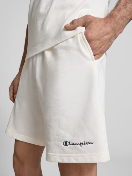 Männermodel trägt Shorts mit elastischem Bund und Label-Stitching von CHAMPION in Offwhite, Baumwoll-Mix, Nahaufnahme Oberschenkel.