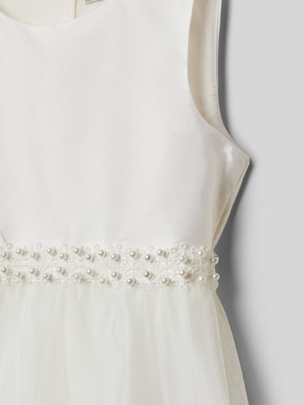 Mädchen trägt Regular Fit Kleid mit Zierbesatz von Une Hautre Couture, Baumwoll-Mix, cremeweiß, Zierschleife, Nahaufnahme Oberkörper.