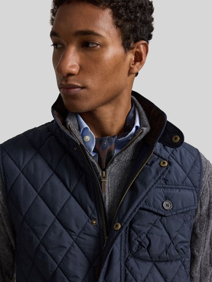 Męski model nosi granatową kamizelkę krój regular fit z naszywką z logo Regular Fit Weste mit Logo-Patch Modell 'BEATON' od Polo Ralph Lauren na szarym tle, zbliżenie górnej części ciała.