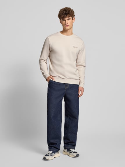 Männermodel trägt Sweatshirt mit Label-Print von Jack & Jones aus Baumwoll-Mix in hellem Beige, Lockerer-Schnitt, Rundhalsausschnitt, Gerippte-Abschlüsse, Rückenlänge 70 cm, Ärmellänge 66 cm, Ganzkörperansicht von vorne.