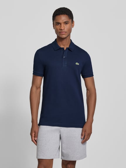 Męski model nosi Slim Fit Poloshirt aus reiner Baumwolle od Lacoste, granatowa koszulka polo, gładka faktura, Ganzkörperansicht von vorne.