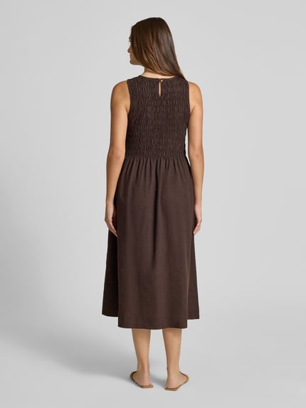 Frauenmodel trägt Midikleid aus Baumwoll-Leinen-Mix mit Eingrifftaschen von Smith and Soul, braun, taillierte Passform, Ganzkörperansicht Rückansicht. Rückenlänge bei Größe S: 120 cm, Brustweite bei Größe S: 36 cm, Rundhalsausschnitt, rückseitiger Schlüsselloch-Ausschnitt, feine Struktur.