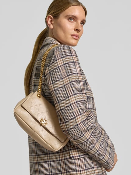Frauenmodel trägt Shoulder Bag mit Klickverschluss von Tory Burch in Beige mit Steppnähten und Kettenschulterriemen, Nahaufnahme Oberkörper.