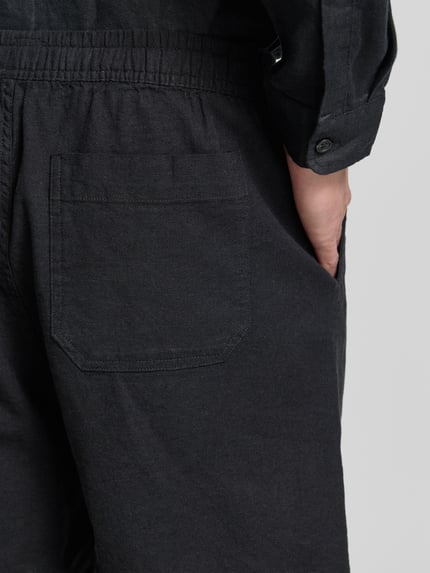 Männermodel trägt Leinenshorts mit elastischem Bund von GAP aus Leinen-Baumwoll-Mix, Loose-Fit, schwarze Farbe, Detailaufnahme Rückansicht. Bundweite 42 cm, Innenbeinlänge 17 cm, Gesäßtasche und Eingrifftaschen.