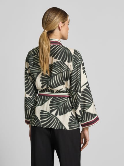 Modelka nosi Kaftan aus Viskose-Mix mit floralem Allover-Print od Christian Berg Woman Selection, kremowy z czarnym wzorem liści, taillierter krój, zdejmowany pasek, długość tyłu w rozmiarze 36: 66 cm, szerokość w rozmiarze 36: 60 cm, długość rękawa w rozmiarze 36: 48 cm, widok całej sylwetki od tyłu.
