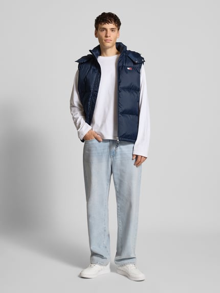 Mannenmodel draagt Regular Fit Daunenweste mit abnehmbarer Kapuze van Tommy Jeans, donkerblauw, staande kraag, label patch, zijzakken, regular fit, unicolor, voorkant volledig zichtbaar, ganzekörperaanzicht van voren.