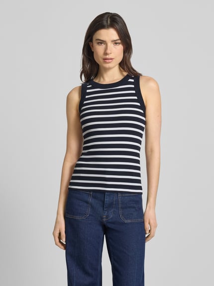 Frauenmodel trägt Tanktop mit Rippenstruktur Modell 'OLINA' von Drykorn aus Reine Baumwolle, eng anliegender Schnitt, Rundhalsausschnitt, Rückenlänge 55 cm bei Größe S, gestreiftes Design, Ganzkörperansicht von vorne.