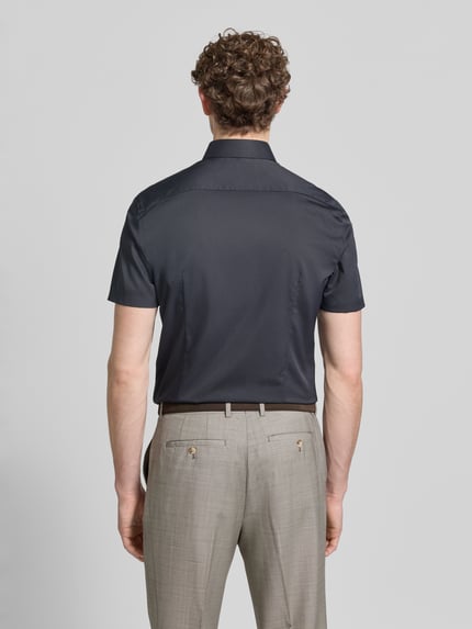 Männermodel trägt Slim Fit Business-Hemd mit Kentkragen von Jake*s in Dunkelblau, glatte Textur, angeschnittener Kentkragen, Kurärmelig, Elastischer-Material-Mix, Ganzkörperansicht Rückansicht. Rückenlänge 80 cm, Schulterbreite 45 cm, Ärmellänge 25 cm.