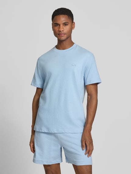Männermodel trägt Regular Fit T-Shirt aus reiner Baumwolle von Lacoste in hellblau, unifarben, Rundhals, kurzarm, Feinstrick, Ganzkörperansicht von vorne.
