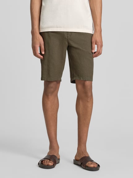 Männermodel trägt Bermudas aus Leinen-Mix mit französischen Eingrifftaschen von Lindbergh in Oliv, Struktur fein, Ganzkörperansicht von vorne. Bundweite bei Größe M: 43 cm, Innenbeinlänge 24 cm, Leinen-Baumwoll-Mix, Straight, Elastischer Bund mit Kordelzug, Knopf- und Reißverschluss, Gesäßtaschen.