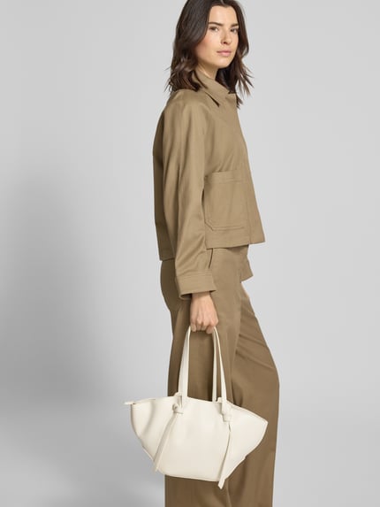 Frauenmodel trägt Shopper mit Label-Detail Modell 'RYD' von Seidenfelt in Beige, Hauptfach mit Reißverschluss, Schulterriemen, Ganzkörperansicht von vorne. Breite 40 cm, Länge 23 cm, Tiefe 12 cm, Riemenlänge 59 cm.