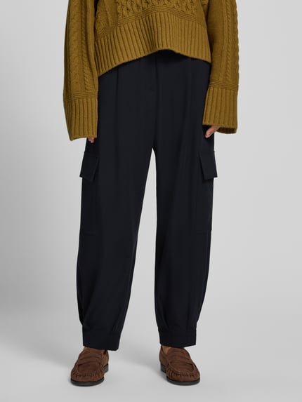 Frauenmodel trägt Cargo-Hose mit weitem Bein – curated by Vera van Erp von Style Icon Collection, schwarze Stoffhose im Loose Fit, Material-Mix mit Viskose-Anteil, französische Eingrifftaschen, Pattentaschen, Gesäßleistentaschen, Knopf- und Reißverschluss, Struktur grob und glatt, Bundweite 37 cm, Innenbeinlänge 68 cm, Nahaufnahme Unterkörper von vorne.