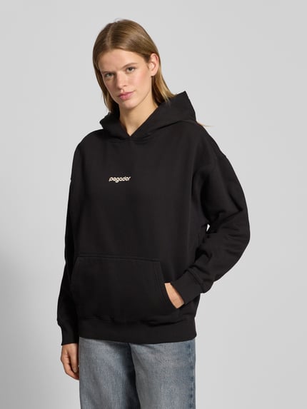 Vrouwenmodel draagt zwarte Oversized Hoodie met kangoeroezak model 'AVERSA' van Pegador, katoenmix, logo, vooraanzicht bovenlichaam.