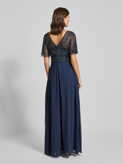 Frauenmodel trägt Abendkleid mit Perlen und Pailletten von Christian Berg Cocktail, A-Linie, Maxikleid, 2-in-1-Look, Rückenlänge 156 cm, Brustweite 45 cm, Ärmellänge 28 cm, Textur aus schimmernden Pailletten, fließender Stoff in Dunkelblau, Ganzkörperansicht Rückansicht.
