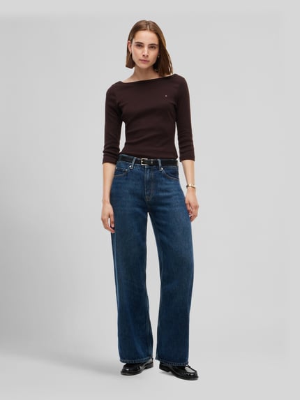Frauenmodel trägt Slim Fit Langarmshirt aus reiner Baumwolle von Tommy Hilfiger in Dunkelbraun mit glatter Textur, Ganzkörperansicht von vorne, Damen T-Shirt von Tommy Hilfiger.