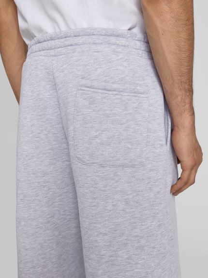 Männermodel trägt Sweatshorts mit Logo-Print van REVIEW, materiaalmix met katoen, loose fit, elastische band, logoprint, detailaufnahme achterzijde.
