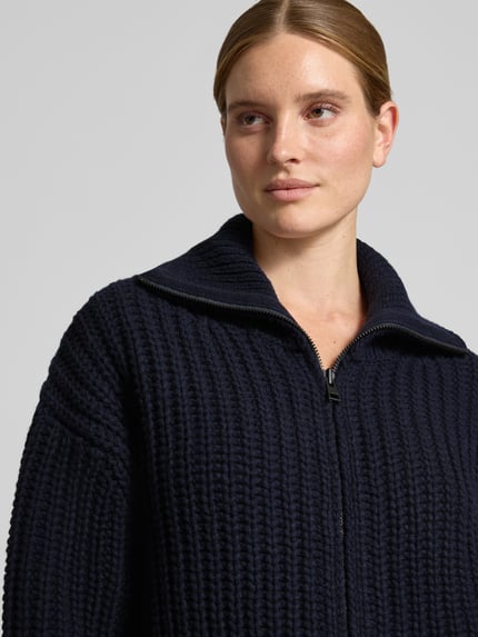 Frauenmodel trägt Strickjacke aus Wolle mit Umlegekragen von Closed in Dunkelblau, Grobstrick, Zweiwege-Reißverschluss, Nahaufnahme Oberkörper.
