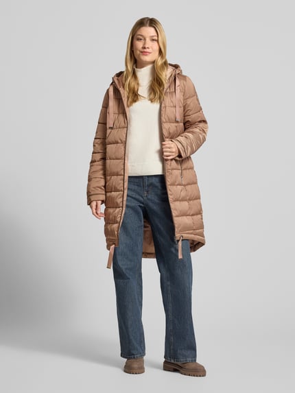 Frauenmodel trägt Steppmantel mit Reißverschlusstaschen von monari in Beige, gerade Passform mit Kapuze, Zweiwege-Reißverschluss, Ganzkörperansicht von vorne.