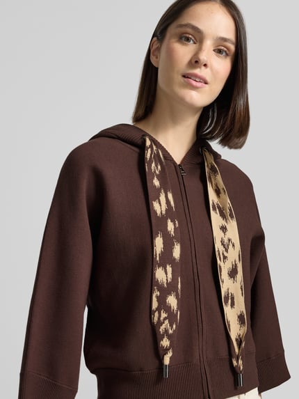 Frauenmodel trägt Strickjacke mit Kapuze von Marc Cain in Braun mit Animal Print Kordeln und gestreiftem Innenfutter, Nahaufnahme Oberkörper.