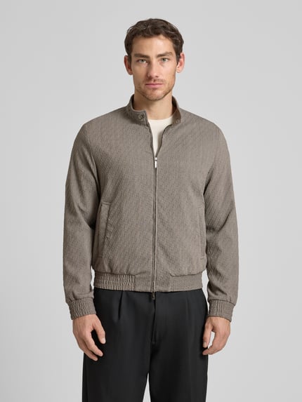 Männermodel trägt Jacke aus Schurwoll-Mix mit Zweiwege-Reißverschluss von Emporio Armani in Grau, strukturierte Oberfläche, Ganzkörperansicht von vorne. Regular Fit, Stehkragen, Eingrifftaschen, elastische Bündchen, dezente Textur, Rückenlänge 63 cm, Schulterbreite 45 cm, Brustweite 53 cm, Ärmellänge 67 cm.