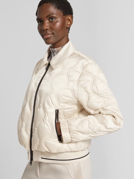 Frauenmodel trägt Steppjacke mit Umlegekragen und Reißverschlusstaschen von Marc Cain in hellem Beige mit sichtbarer Steppstruktur, Regular Fit, Reißverschluss und Reißverschlusstaschen, Ganzkörperansicht von vorne. Rückenlänge, Schulterbreite, Brustweite und Ärmellänge gemäß Größe 36.