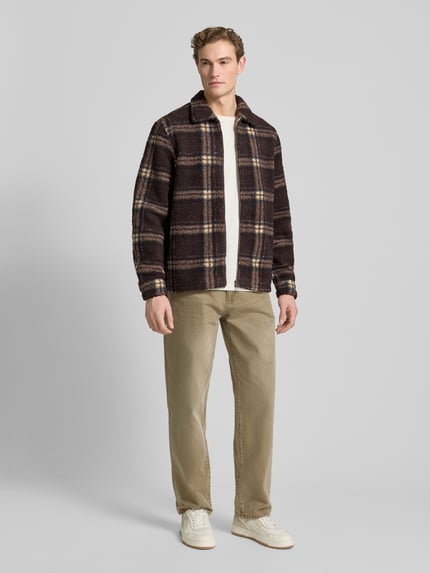 Männermodel trägt Hemdjacke mit Reißverschluss von Forét aus braun kariertem Teddyfell, Regular Fit, Kentkragen, Ganzkörperansicht von vorne.