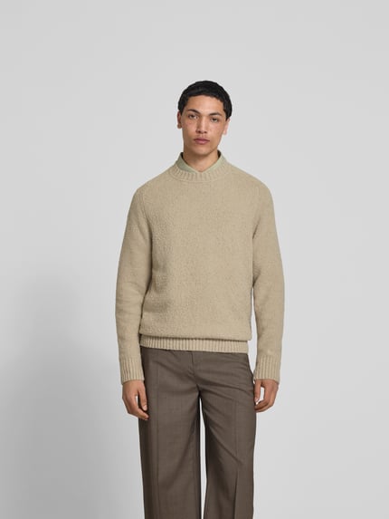 Męski model nosi Relaxed Fit Pullover in Strick-Optik od Forét, elastyczna mieszanka bawełny, bouclé, beżowy, okrągły dekolt, widok od przodu, ujęcie całej sylwetki.