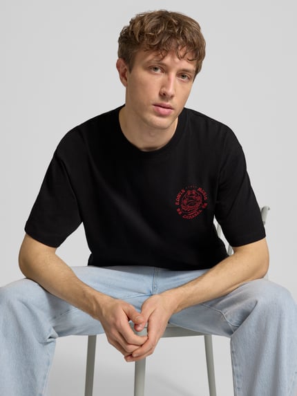 Männermodel trägt schwarzes T-Shirt aus reiner Baumwolle Modell 'MUSIC CHANNEL' von Edwin mit rotem Print, Nahaufnahme Oberkörper. Gerader Schnitt, Rundhalsausschnitt.