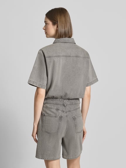 Frauenmodel trägt Regular Fit Playsuit in Denim-Optik Modell 'Fillipa' von JJXX aus Reine Baumwolle, 5-Pocket-Design, Kurzärmelig, Umlegekragen, Knopfleiste, Brusttasche, Rückenlänge bei Größe S: 93 cm, Brustweite: 52 cm, Ärmellänge: 26 cm, Gesamtlänge: 88 cm, Innenbeinlänge: 17 cm, einfarbig grau mit strukturierter Oberfläche, Ganzkörperansicht Rückansicht.