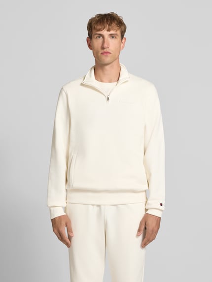 Mężczyzna model nosi Sweatshirt mit Label-Details od Champion, mieszanka bawełny, prosty krój, kołnierz zapinany, wpuszczane kieszenie, długość tyłu w rozmiarze M: 72 cm, długość rękawów w rozmiarze M: 71 cm, jasny kolor, gładka tekstura, Ganzkörperansicht von vorne.