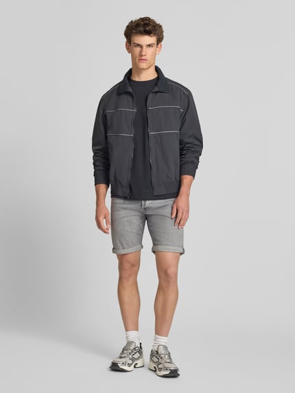 Männermodel trägt Regular Fit Jeansshorts mit Umschlag Modell 'RICK' von Jack & Jones aus Baumwoll-Elasthan-Mix, Eingrifftaschen, Ganzkörperansicht von vorne. Bundweite bei Größe M: 42 cm, Innenbeinlänge bei Größe M: 21 cm.
