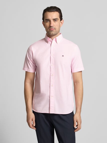 Männermodel trägt Regular Fit Freizeithemd aus reiner Baumwolle von Tommy Hilfiger in zartem Rosa mit Button-Down-Kragen, Optik: Allover-Muster, Mini-Hahnentritt, Logo-Stitching, Popeline, Kurzarm, Ganzkörperansicht von vorne.
