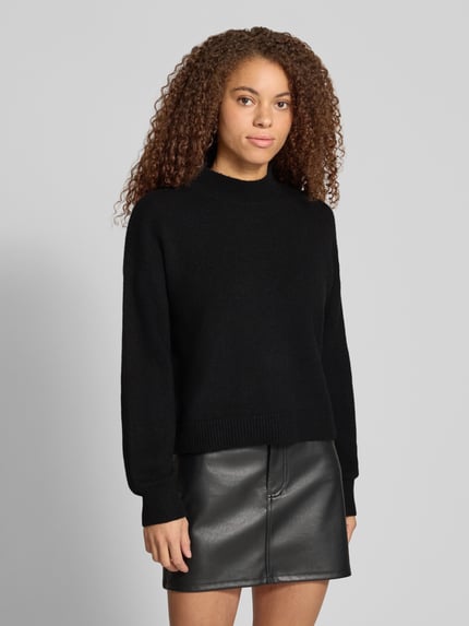 Frauenmodel trägt Pullover mit Mock Neck Modell 'PCMALOU' von PIECES in Schwarz, unifarben, Strickoptik, gerippte Abschlüsse, Ganzkörperansicht von vorne.