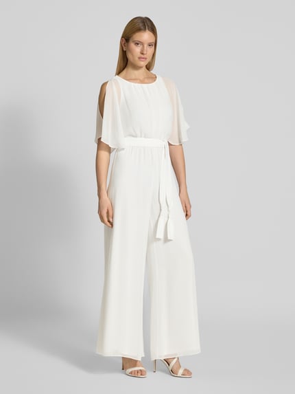 Vrouwenmodel draagt Jumpsuit aus fließendem Stoff mit Bindegürtel van Vera Mont in wit chiffon met wijde benen, strikceintuur, ruglengte maat 36: 146 cm, borstwijdte: 33 cm, mouwlengte: 30 cm, totale lengte: 147 cm, binnenbeenlengte: 81 cm. Volledige lichaamsaanzicht vooraan.