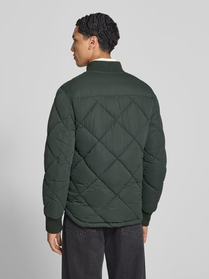 Männermodel trägt Regular Fit Steppjacke mit opstaande kraag van Superdry, donkergroen met Stiksels, Steekzakken, elastische mouwboorden, ritssluiting, Ruglengte maat M 69 cm, schouderbreedte 46 cm, borstwijdte 58 cm, mouwlengte 59 cm, doorgestikte textuur, Ganzkörperansicht Rückansicht