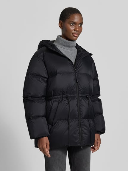 Kobiece modelka ma na sobie czarną 'Jacke mit Kapuze und Zweiwege-Reißverschlus' od Closed, prosty krój, kaptur, trok w talii, wpuszczane kieszenie, dzianinowe zakończenia rękawów, długość tyłu w rozm. S: 77 cm, szerokość ramion: 53 cm, szerokość w rozm. S: 62 cm, długość rękawów: 63 cm, widok całej sylwetki z przodu.