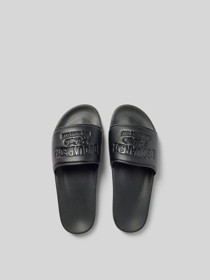Produktfoto, schwarze Slides mit Label-Prägung von Dsquared2, abgerundete Form, offene Ferse, Strukturmuster, glatte Sohle.