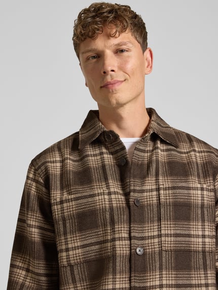 Männermodel trägt Freizeithemd mit durchgehender Knopfleiste von Selected Homme im karierten Allover-Muster, Brauntöne, Nahaufnahme Oberkörper.