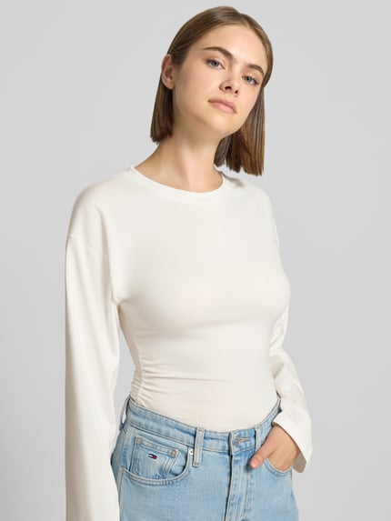 Modelka nosi bluzkę z długim rękawem z mieszanki bawełny, taliowany krój, okrągły dekolt, Longsleeve aus Baumwoll-Mix Modell 'Paloma' od JJXX, długość tyłu w rozmiarze S: 57 cm, jasny kolor, gładka tekstura, widok całej sylwetki z przodu.