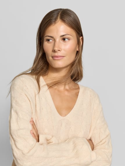 Frauenmodel trägt Relaxed Fit Pullover aus reiner Baumwolle von MYON in Beige, V-Ausschnitt, Strick-Optik, Nahaufnahme Oberkörper