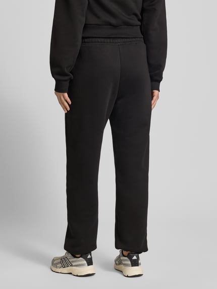 Männermodel trägt Basic Sweatpant mit Bündchen am Saum und seitlichen Taschen von Review, czarny kolor, bawełniany materiał, luźny krój, elastyczne ściągacze, logo haftowane, kieszenie boczne, widoczny label print, długość nogawki wewnętrznej S: 74 cm, Ganzkörperansicht Rückansicht.