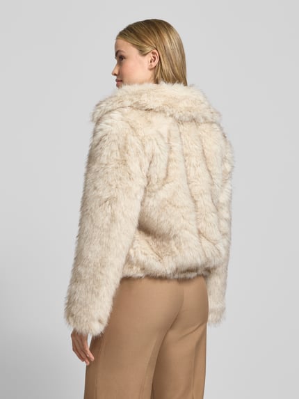 Młodzieżowy model nosi Jacke aus Kunstfell mit Reißverschluss od Stefanel, kremowy kolor, regular fit, widok całej sylwetki z tyłu.