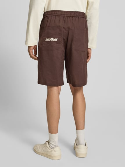 Männermodel trägt Leinenshorts mit elastischem Bund und Tunnelzug von ANOTHER COTTON LAB in Braun, Regular-Fit, Ganzkörperansicht Rückansicht. Reines Leinen, Herren Shorts, Bundweite 42 cm, Innenbeinlänge 20 cm, klare Struktur mit sichtbaren Nähten.