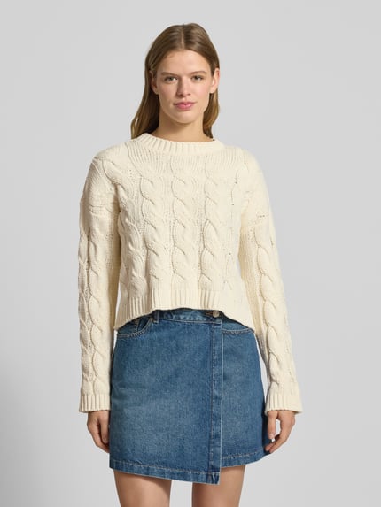 Frauenmodel trägt Regular Fit Sweter z dzianiny z ściegiem warkoczowym Model 'ELLY' od Only, efekt: jednolity kolor, skrócony krój, okrągły dekolt, prążkowane zakończenia, wykończenie: dzianina, długi rękaw, Ganzkörperansicht von vorne.
